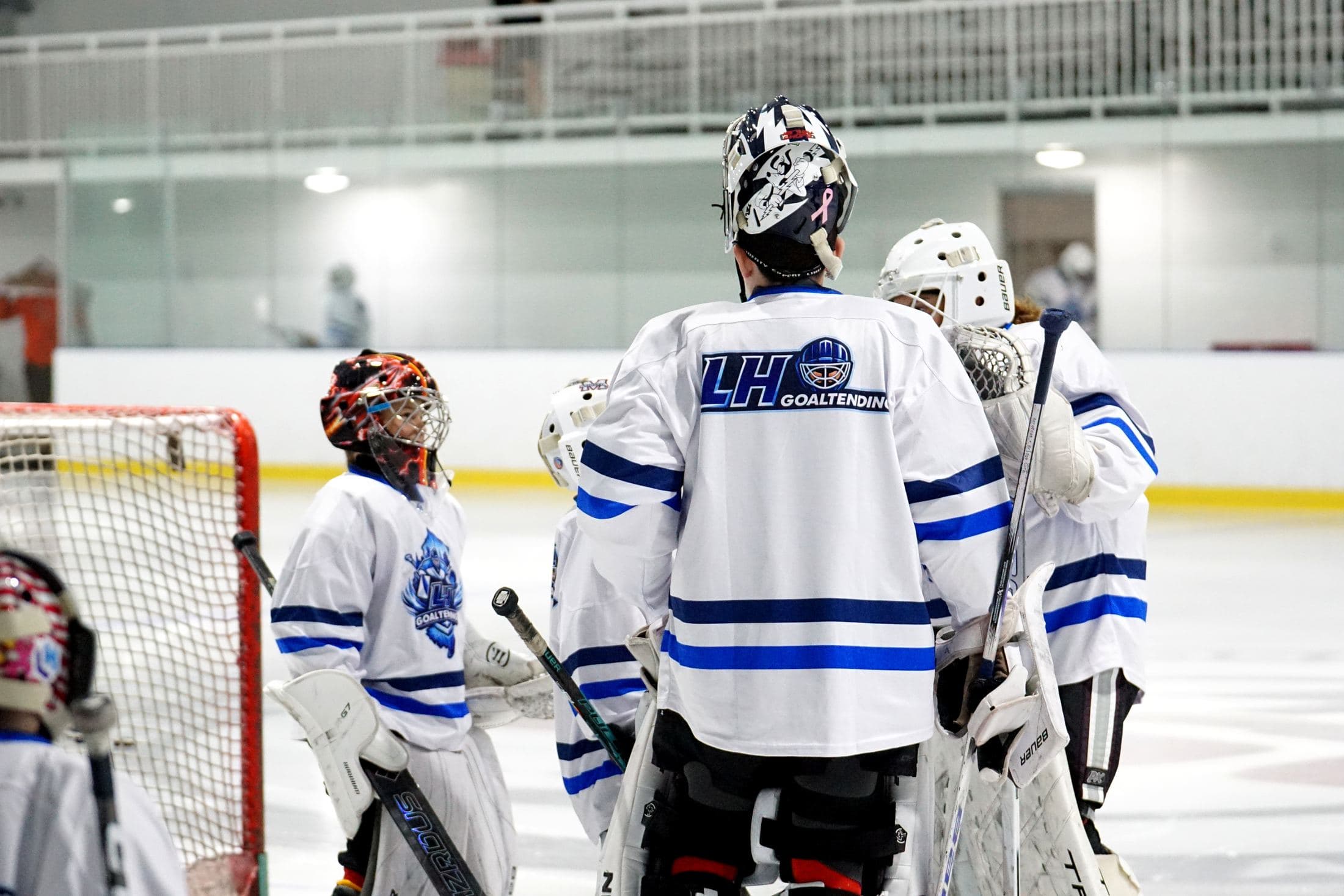 Goalies in LH Goaltending jerseys gathered at the net during camp